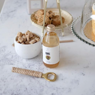 Brass Bottle Opener with Rattan Handle pictured in front of a table of sweets