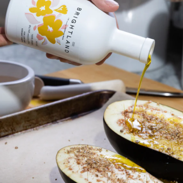 Brightland Basil Olive Oil being poured onto a seasoned eggplant