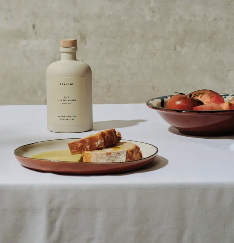 Branche Number Two Olive Oil pictured behind a plate with bread and olive oil and next to a bowl with tomatoes